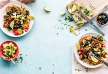 Colorful Mexican salad with avocado, black beans, and lime on a light blue surface.