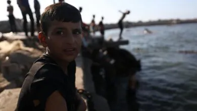 A boy sits by the water as children play, creating a lively scene in Gaza's coastal area.
