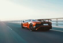Dynamic shot of a red sports car speeding on an open coastal highway during the day.