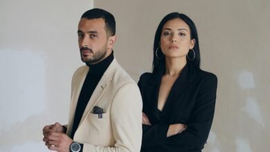 A man and woman posing confidently in stylish formal wear against a textured wall.