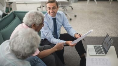 Consultant discussing financial plans with senior clients in a modern office setting, using documents and a laptop.