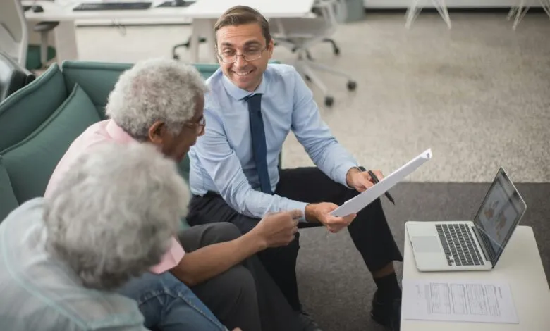 Consultant discussing financial plans with senior clients in a modern office setting, using documents and a laptop.