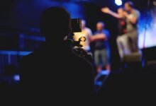 A cameraman films a live concert performance, capturing the dynamic stage action.