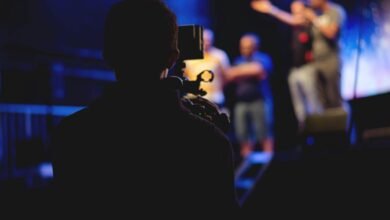 A cameraman films a live concert performance, capturing the dynamic stage action.