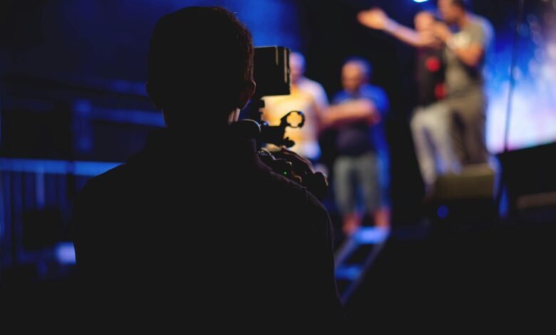 A cameraman films a live concert performance, capturing the dynamic stage action.